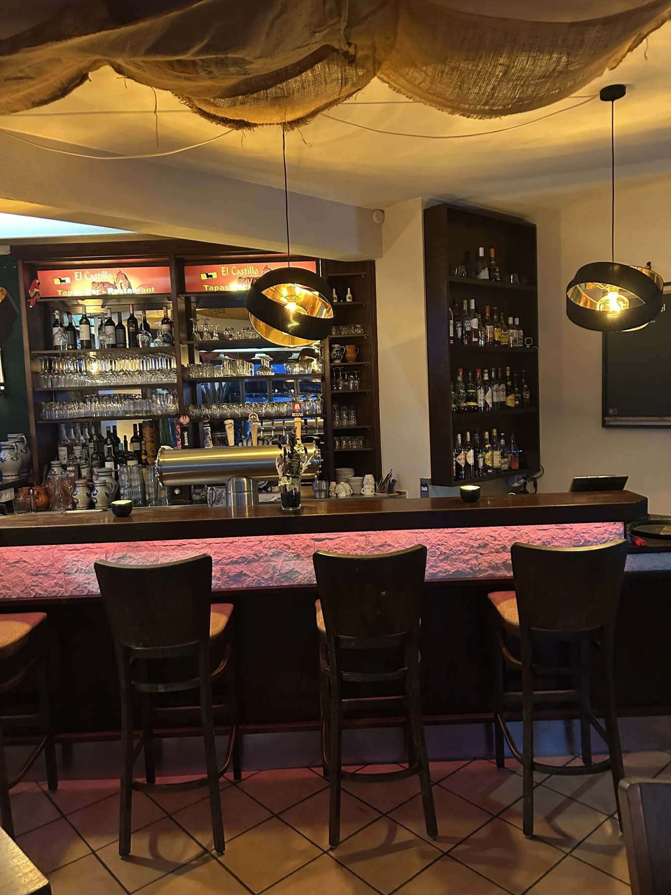 Die warme beleuchtete Bar im El Castillo mit Hockern und Weinregalen
