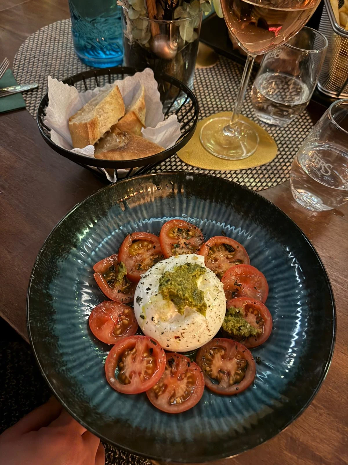 Burrata mit Tomaten und grünem Pesto auf einem dunklen Teller