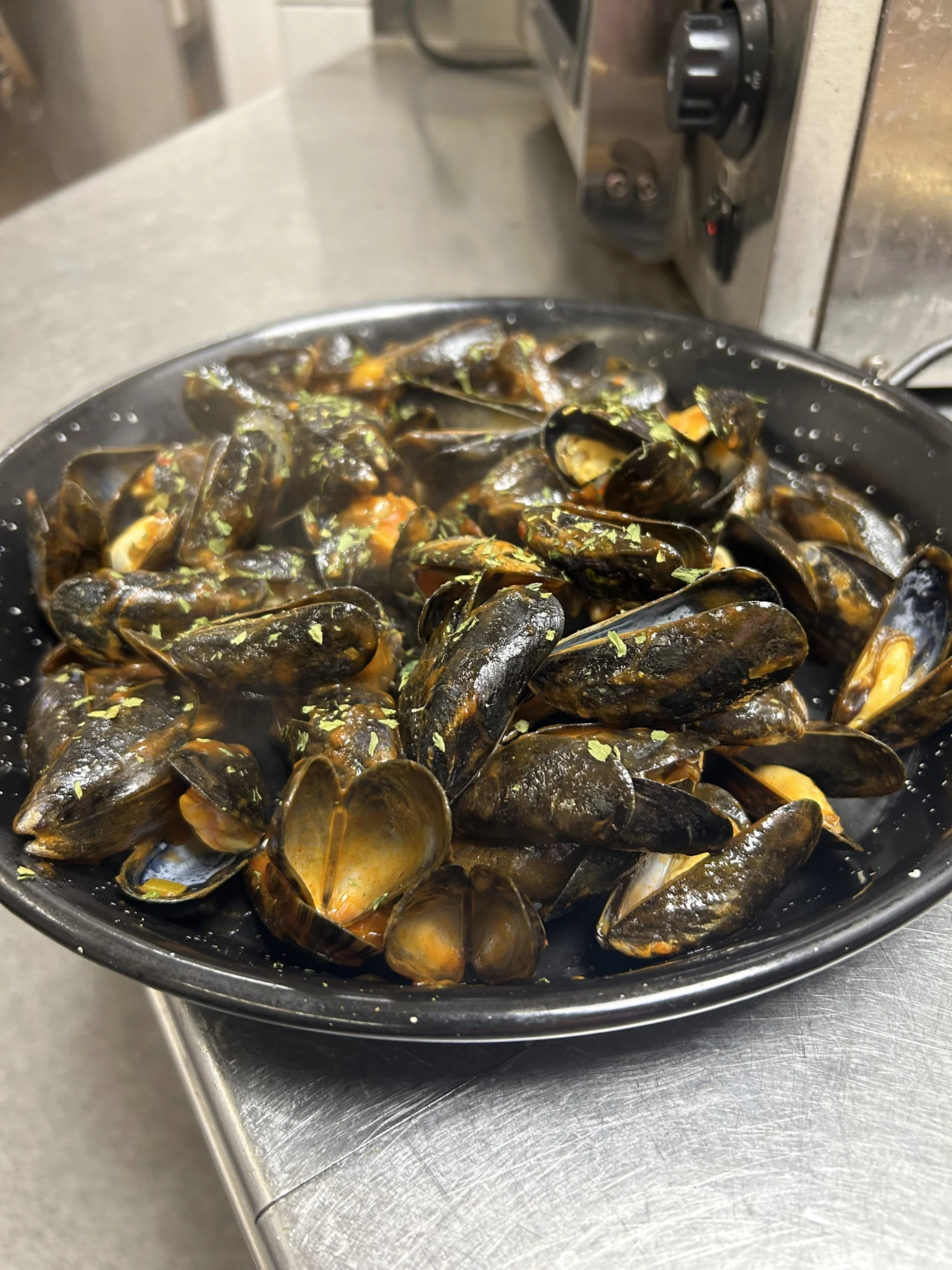Große schwarze Pfanne mit gegarten Miesmuscheln und Kräutern