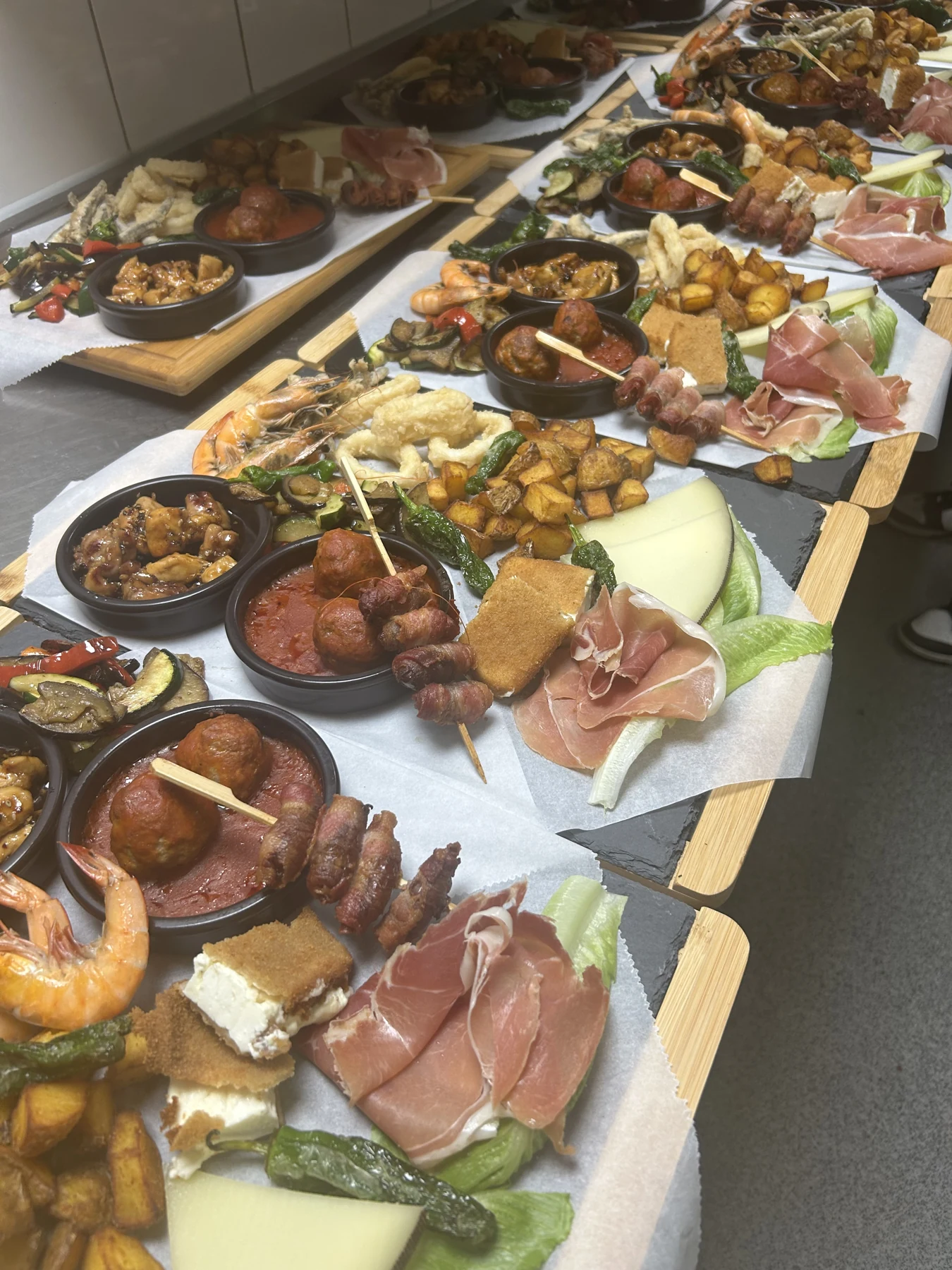Mehrere Tapasplatten mit Garnelen, Schinken, Gemüse, Kartoffeln und kleinen Schälchen