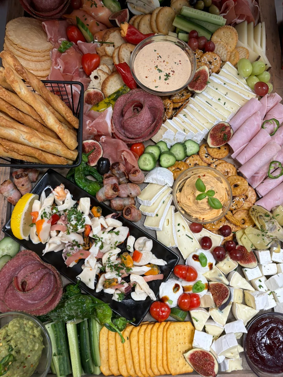 Bunt angerichtete Platte mit Käse, Schinken, Gemüse, Dips und Meeresfrüchten
